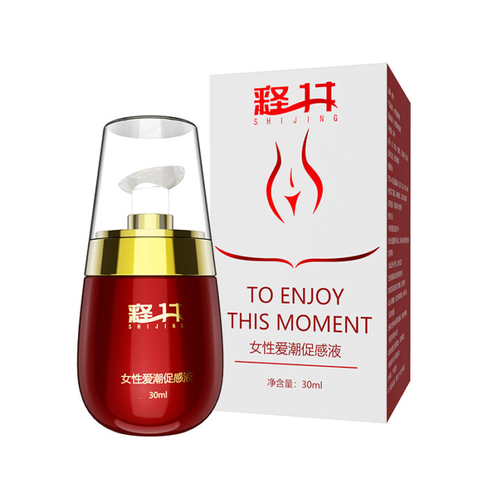 A red cosmetic bottle of Female Orgasm Enhancer 30ml Love Tide Arousal Liquid, featuring a transparent cap and gold accents, is placed in front of a matching red and white box. The box and bottle showcase Chinese characters along with the English phrase "To Enjoy This Moment." The bottle's capacity is 30ml.